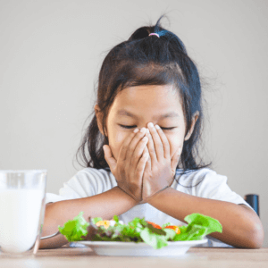 Girl covering mouth with plate of food in front of her